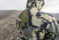 Back of hunter on a mountain top wearing the KUIU Kutana Storm Shell Jacket in Verde Camouflage