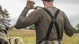 Male hunter adjusting his Proximity Insulated Pant suspender's and whitetail deer hunting mid-layers in an open field.
