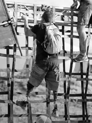 Black-and-white image of several veterans climbing a cargo-net in an obstacle course.