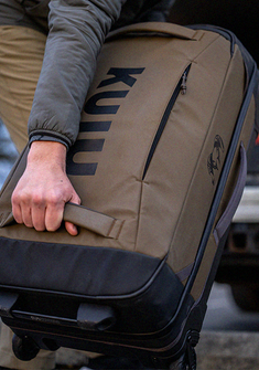 Close-up of a person carrying a Waypoint Roller Bag in Bourbon Brown, gripping a side handle.