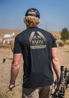 A man wearing KUIU Ultralight Hunting T-Shirt walks in a dry field while carrying a bow.