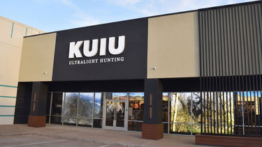 The exterior of the KUIU Houston store under a blue sky, featuring a prominent black and beige facade with the white text 'KUIU ULTRALIGHT HUNTING' on the main sign.