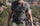 A man wearing a backpack and holding a bow in a rocky, desert environment.