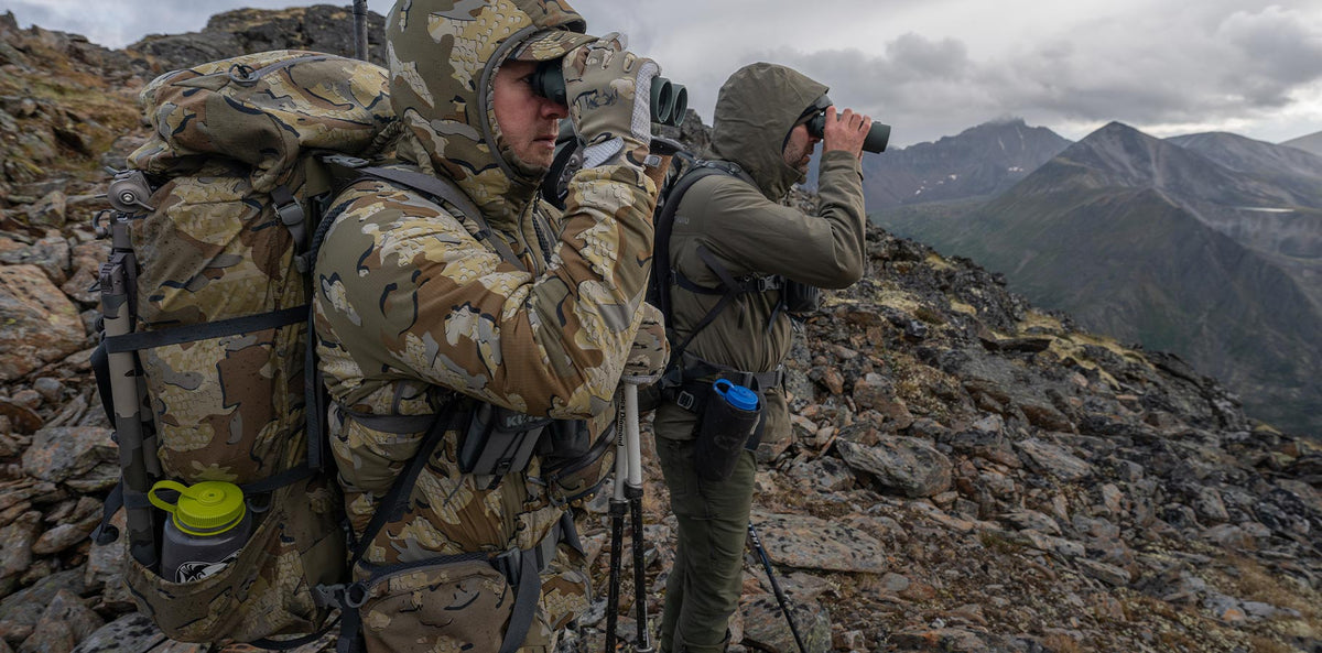 Two men standing on a mountain top and glassing.