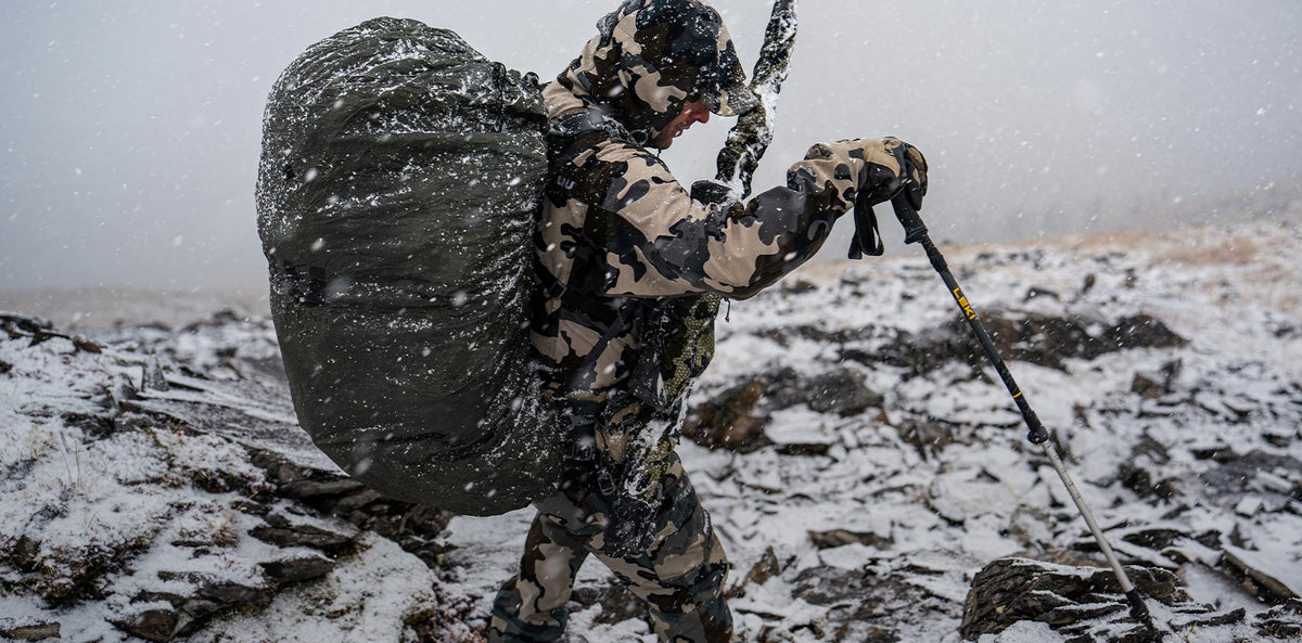 A hunter backpacking across a snowy mountain.