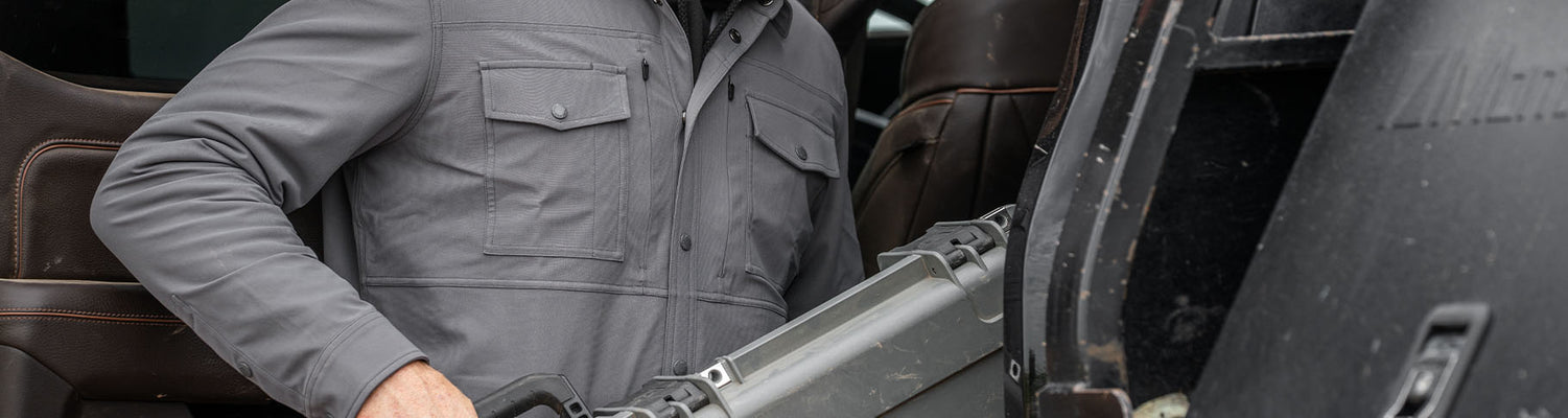 Close-up of man wearing the Tour Shirt Jacket in Castle Rock color lifting a KUIU Hard Case in Stone Grey into the back seat of vehicle