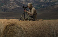 Hunter in Gila LS hoodie in bone brown sitting on top of hay bale looking for antelope