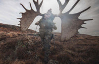 Hunter in Valo camouflage packing out a skinned moose skull  uphill away from the camera