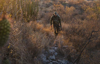 Bowhunter in valo camoufalge walking upslope while carrying his bow