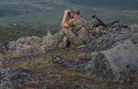 Hunter in Valo camouflage seated and looking through binoculars