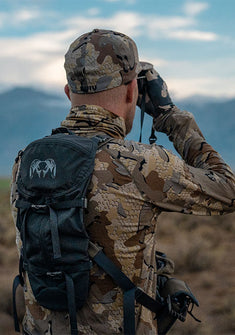 Back of hunter scanning the landscape with optics 