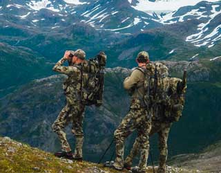 Two hunters in Verde camouflage gear and ICON 6 Packs standing on a mountain with snow-capped peaks in the background.