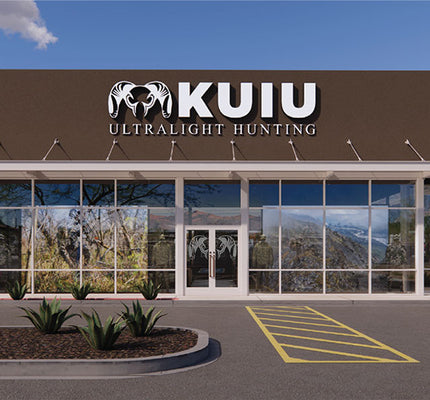 Tempe, Arizona front exterior of a KUIU Ultralight Hunting retail store with a brown facade, large glass windows, and a parking lot under a blue sky.