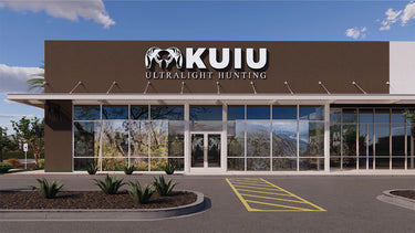 Tempe, Arizona front exterior of a KUIU Ultralight Hunting retail store with a brown facade, large glass windows, and a parking lot under a blue sky.